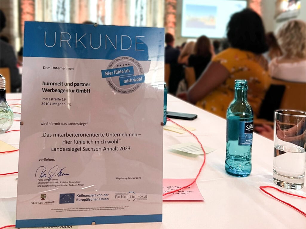 Urkunde des Landessiegels "Da mitarbeiterorientierte Unternehmen - Hier fühle ich mich wohl" 2023 auf dem Tisch bei der Verleihung.