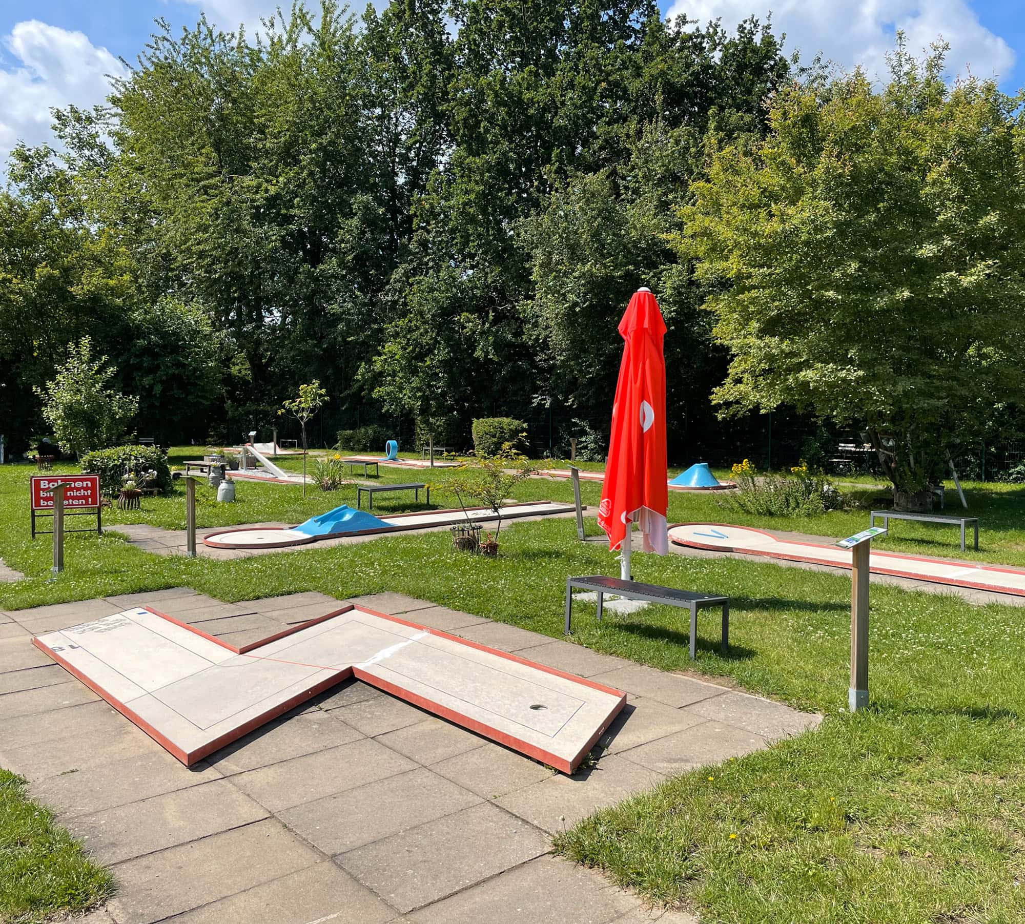 Hupa Teamevent Minigolf 1 Blick auf die Bahnen der Minigolfanlage draußen an einem sonnigen Tag.