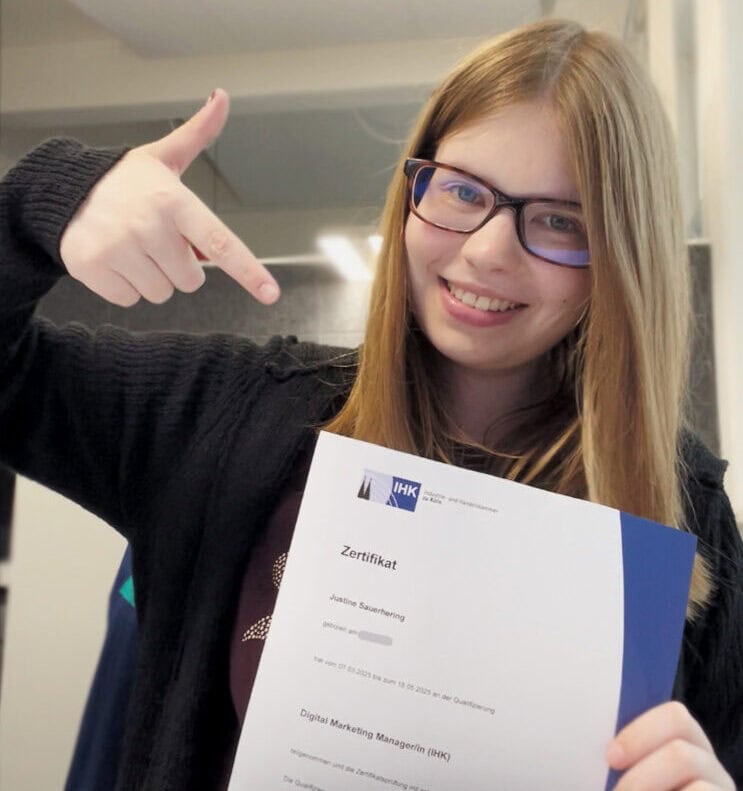 Weiterbildung Justine 2025 Justine, die stolz auf ihr Weiterbildungs-Zertifikat von der IHK zur "Online Marketing Managerin" zeigt.