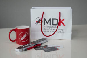 Professionelle Werbeartikel für die MDKr GmbH: auf einem Tisch liegen eine Tasse, Visitenkarten, ein Stift, ein Zollstock und eine Tüte um kreativ ausgestaltetem Corporate Design