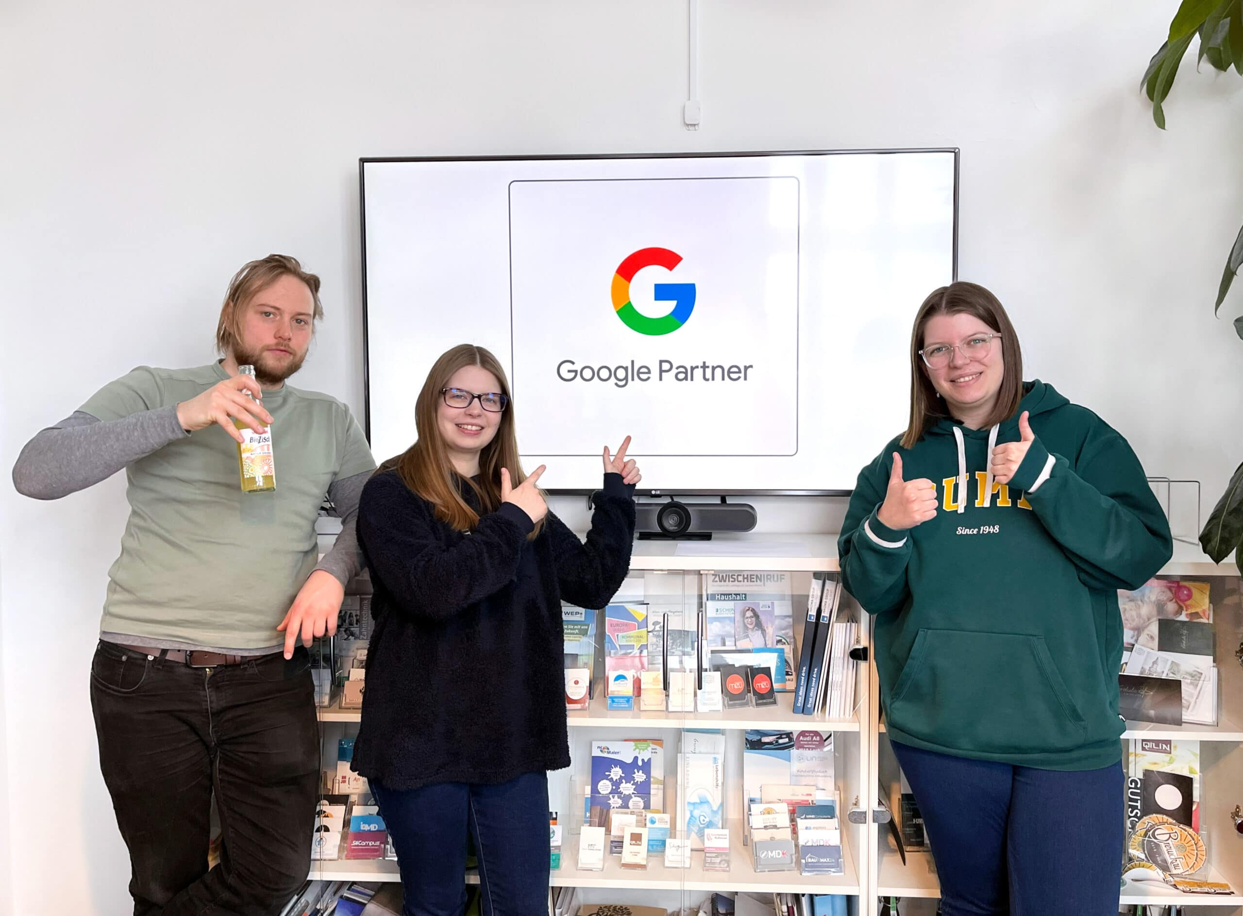 Unser hupa Team steht vor einem großen Bildschirm, auf dem das Google Partner Logo zu sehen ist.