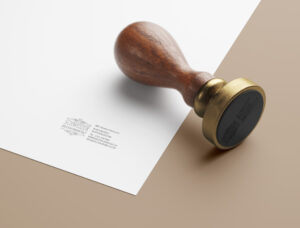Ein Stempel und ein Blatt Papier liegen auf einem Tisch. Auf dem Papier wurde das Logo und Kontaktdaten gestempelt